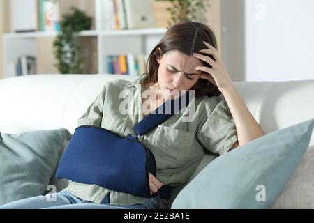 Besorgt behinderte Frau mit gebrochenem Arm beschweren sitzen auf einem Couch im Wohnzimmer zu Hause Stockfoto