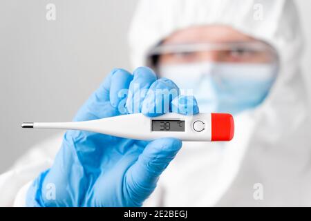 Digitales oder elektronisches Thermometer mit einer Temperatur von 38 grad celsius in der Hand des Arztes. Arzt oder Krankenschwester in schützendem PSA-Anzug, Gesichtsmaske, Sicherheit Stockfoto