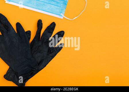 Schwarze Handschuhe mit Einwegmaske auf farbigem Hintergrund. Heilmittel gegen Coronavirus. Draufsicht mit Kopierbereich. Stockfoto