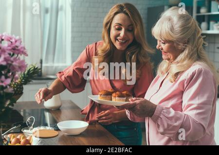 Cincematic Bild von einer älteren Frau und ihre Tochter Backen und Kochen Essen in ihrer schönen Küche. Großmutter bereitet Kuchen und Süßigkeiten für die Stockfoto
