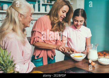 Cincematic Bild von einer älteren Frau und ihrer Tochter und Enkelin Backen und Kochen Essen in ihrer schönen Küche. Großmutter bereitet Kuchen und Stockfoto