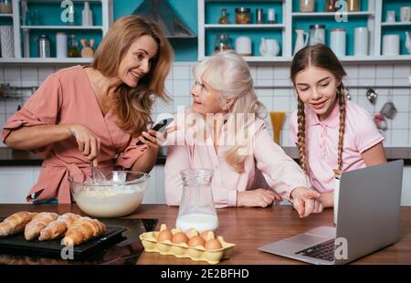 Cincematic Bild von einer älteren Frau und ihrer Tochter und Enkelin Backen und Kochen Essen in ihrer schönen Küche. Großmutter bereitet Kuchen und Stockfoto