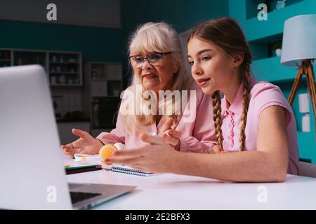Filmisches Bild einer Großmutter und einer Enkelin, die zusammen Hausarbeiten machen. Mutter, die dem Kind hilft, das von zu Hause studiert, während 2020 die Sperre Stockfoto