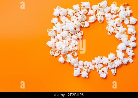 Verstreutes Popcorn in Herzform auf orangefarbenem Hintergrund. Zeit, die von Angehörigen verbracht wird. Film und Popcorn. Stockfoto