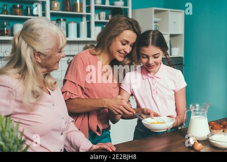 Cincematic Bild von einer älteren Frau und ihrer Tochter und Enkelin Backen und Kochen Essen in ihrer schönen Küche. Großmutter bereitet Kuchen und Stockfoto