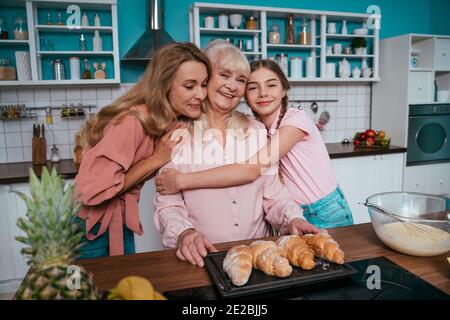 Cincematic Bild von einer älteren Frau und ihrer Tochter und Enkelin Backen und Kochen Essen in ihrer schönen Küche. Großmutter bereitet Kuchen und Stockfoto