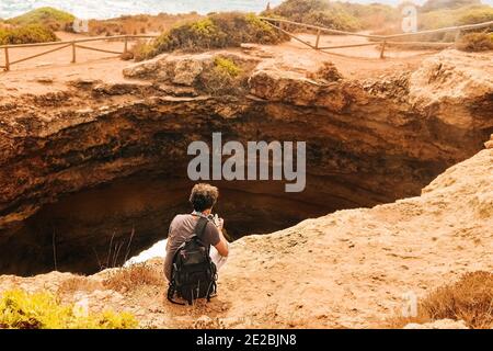 Felsen am berühmten Benagil Strand in Portugal sitzt ein Kerl in der Nähe einer Schlucht in einer Höhle und macht Fotos Stockfoto