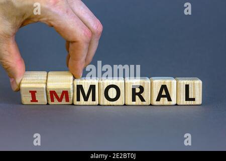 Moralisches oder unmoralisches Symbol. Hand dreht Würfel und ändert das Wort "unmoralisch" in "oral". Schöner grauer Hintergrund. Business und moralische oder unmoralische Konzept. Stockfoto