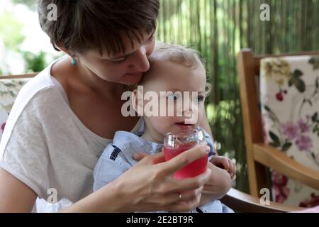 Kleinkind trinkt Saft von Mutterhänden im Café Stockfoto