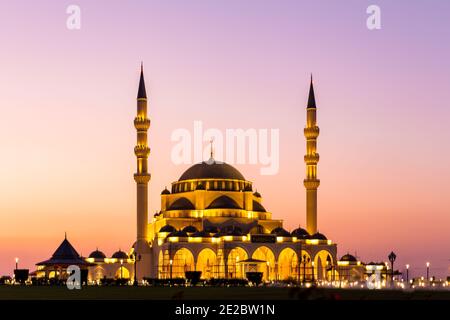 Neue Sharjah Moschee, die größte Moschee im Emirat Sharjah, die Vereinigten Arabischen Emirate, mit rosa Himmel Sonnenuntergang und Fassade Beleuchtung. Stockfoto