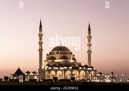 Neue Sharjah Moschee, die größte Moschee im Emirat Sharjah, die Vereinigten Arabischen Emirate, mit rosa Himmel Sonnenuntergang und Fassade Beleuchtung. Stockfoto