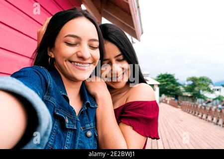 Junge glückliche hispanische Freundinnen zusammen mit Klammern lächelnd und Ein Selfie machen Stockfoto