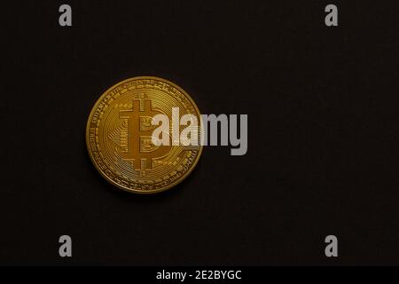 Single golden glänzend wertvolle Bitcoin Vorderansicht mit schwarzem Hintergrund Links und Mitte Stockfoto