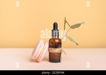 Tropfflasche aus Glas mit Pipette mit schwarzer Gummispitze mit Eukalyptus und rosa Makronen auf dem schönen farbigen Hintergrund. Naturhautkonzept. Stockfoto