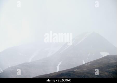 Steile verschneite Hänge von felsigen Bergen mit scharfen Gipfeln versteckt Im Winter unter grauem nebligen Himmel Stockfoto