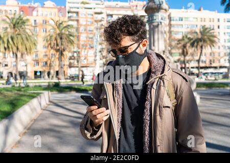 Mann mit Gesichtsmaske und Sonnenbrille ruft am Telefon Auf der Straße Stockfoto