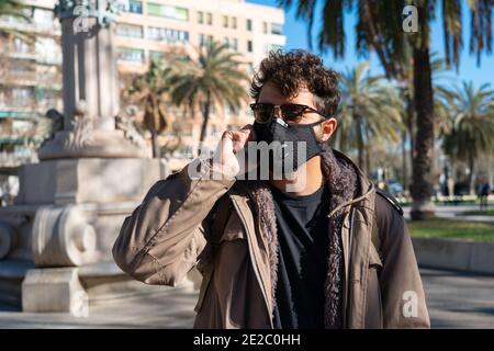 Mann mit Gesichtsmaske und Sonnenbrille ruft am Telefon Auf der Straße Stockfoto