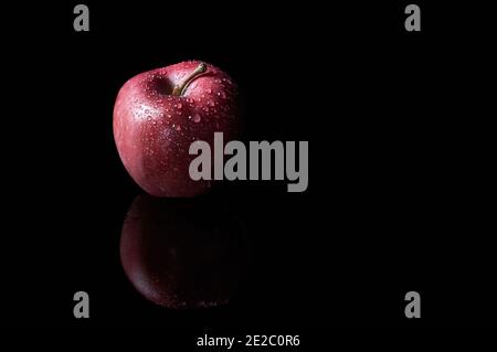Roter Apfel auf schwarzem Hintergrund mit Wassertropfen Stockfoto