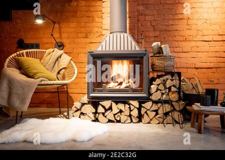 Gemütlicher Kamin mit Feuerholz im Loft-Stil Haus mit Backstein Wand Hintergrund, brennendes Feuer im Kamin, Haus Gemütlichkeit im Winter Stockfoto