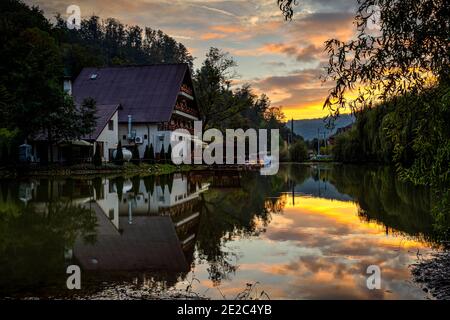 Hütte und dramatischer Himmel bei Sonnenuntergang spiegelt sich im See. Foto aufgenommen am 9. Oktober 2020 in Moneasa, Kreis Arad, Rumänien. Stockfoto