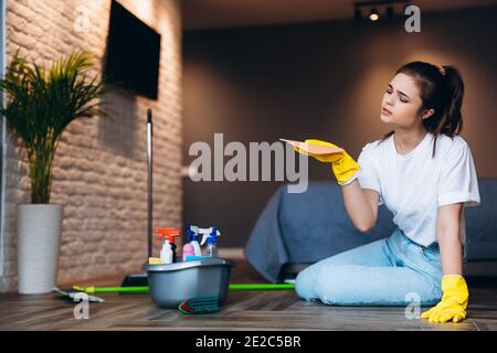Müde Frau in weißem T-Shirt mit dunklen Haaren Reinigung in gelben Gummihandschuhe für den Schutz der Hände und Eimer mit Reinigungsmittel zu Hause. Stockfoto