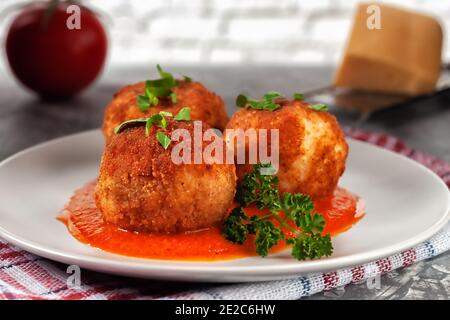 Italienische arancini - Reisbällchen gefüllt mit Käse und Tomaten Sauce in einem Teller auf einem alten Holztisch Stockfoto