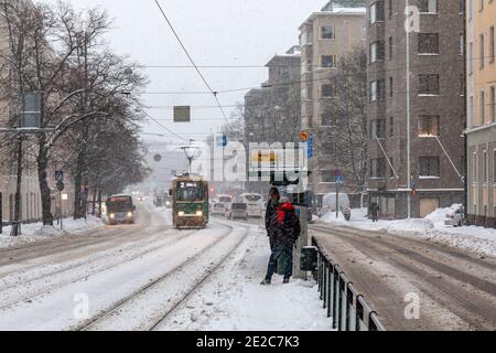 Mannerheimintie Straßenansicht mit Menschen warten auf eine Straßenbahn auf eine Haltestelle im Schneefall. Die Straßenbahn der Linie 2 nähert sich. Taka-Töölön, Helsinki, Finnland. Stockfoto