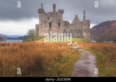 Eine junge Frau nähert sich den historischen Ruinen von Kilchurn Castle in Argyll und Bute in den schottischen Highlands. Stockfoto