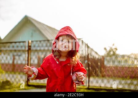 Nettes Mädchen in einer roten Jacke springt in der Pfütze.der Einstellung warmen Sommer oder Herbstsonne. Sommer im Dorf. Stockfoto