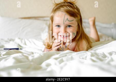 Baby Mädchen zeichnet Hände und Füße mit einem Marker. Kinder spielen im Bett. Morgen zu Hause. Schmutziges Kind. Stockfoto