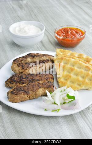 Kebabs mit Pita-Brot, gehackte Zwiebel, Joghurt und Tomatensaucei n Schüsseln auf Holztisch Stockfoto