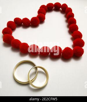 Goldene Eheringe und rotes Herz. Eheringe auf weißem Hintergrund, umgeben vom Herzen. Symbol der Liebe und Hingabe Stockfoto
