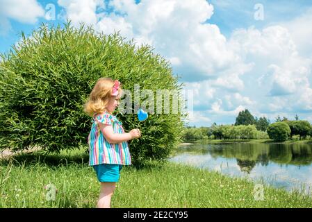 Baby Mädchen mit Lollipop im sonnigen Park. Kinder Kinder spielen im Sommer im Freien, essen Süßigkeiten. Kleinkind mit süßem Snack. Kind mit ungesunder Zucker behandeln. Stockfoto