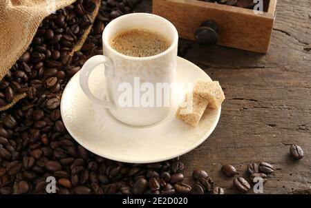 Rustikaler Hintergrund mit Tasse Kaffee Espresso in weißem Porzellan tasse mit gerösteten Kaffeebohnen auf altem Holzhintergrund mit leinentasche Stockfoto