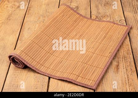 Bambusmatte für Lebensmittel auf einem Holzhintergrund. Eine Seite der Matte ist aufgerollt. Stockfoto