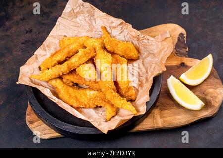 Gebratene Hähnchendipper in schwarzem Eimer mit Sauce auf schwarzem Hintergrund.Hähnchenpanierte Streifen auf einem schwarzen Teller mit Ketchup und pommes frites. Stockfoto