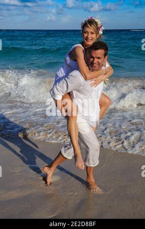 Das frisch verheiratete Paar feiert seine Hochzeit an einem Strand auf der karibischen Insel Mustique. Hand in Hand spritzen sie in die Brandung und schmeißen das Kleid ab. Stockfoto