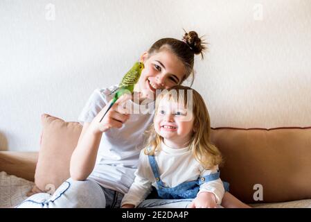 Glückliche Kinder spielen mit einem Papagei am Computer zwei Mädchen zu Hause im Gespräch mit einem Papagei. Haustier. Wellensittiche. Online-Beratung des Tierarztes Stockfoto