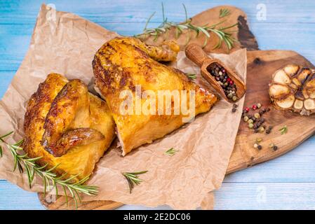 Gegrilltes Hähnchen. Die Hälfte des gebackenen Hähnchens auf dem Papier auf einem hölzernen Brett in der Küche mit Gewürzen und gebackenem Knoblauch Stockfoto
