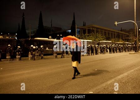 Dame mit rotem Schirm geht vor den Polizeikräften, die die amerikanische Botschaft am 17. November 17 2011 beim jährlichen protestmarsch in Athen, Griechenland bewachen. Die Kundgebung, die von der Polytechnischen Schule beginnt, geht um das Parlament herum und endet weiter nördlich am Mavili Platz vor der US-Botschaft. Insgesamt 78 Personen wurden den ganzen Tag vor, während und kurz nach dem jährlichen protestmarsch vom 17. November in Zentral-Athen anlässlich eines Studentenaufstands im Jahr 1973 festgenommen. Foto von Sophia Petrova/ABACAPRESS.COM Stockfoto