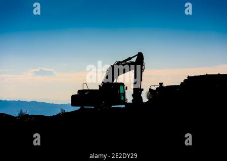 Hinterleuchtete Silhouette eines Baggers auf einem Hügel mit unfokussierten Himmel Hintergrund. Stockfoto