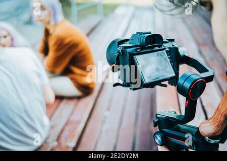 Backstage wie der Bediener mit einer professionellen Kamera auf elektronischem Steadicam arbeitet. Videofilmer nimmt Clips mit Frauen oder Teenagern im Park im Freien auf. Stockfoto