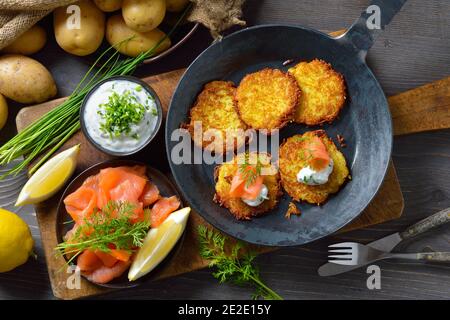 Knusprige Kartoffelpfannkuchen mit geräuchertem Lachs und Schnittlauch-Quark serviert In einer eisernen Pfanne Stockfoto