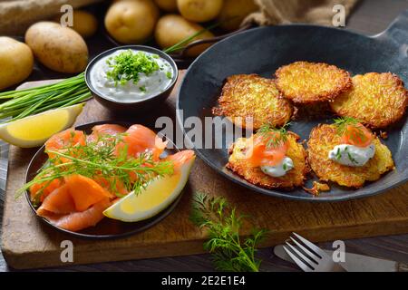 Knusprige Kartoffelpfannkuchen mit geräuchertem Lachs und Schnittlauch-Quark serviert In einer eisernen Pfanne Stockfoto
