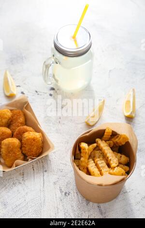 Glas mit Limonade, leckeren Nuggets und pommes Frites in Papierschachteln auf hellem Hintergrund Stockfoto