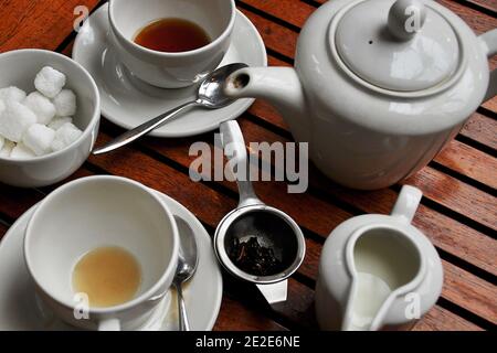 Überblick über einen abgeschlossenen Teeservice für zwei Personen mit leerten Teetassen, einer Teekanne, Zuckerwürfeln, Milchkanne und losem Teesieb auf dem Bistro-Tisch im Freien Stockfoto