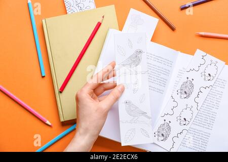 Weibliche Hand mit niedlichen Lesezeichen und Bücher auf farbigem Hintergrund Stockfoto