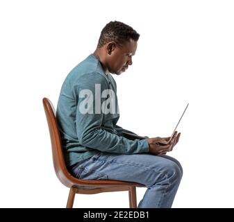 Ein afroamerikanischer Mann mit Buckelwunde und Laptop sitzt auf einem Stuhl gegen Weiß Hintergrund Stockfoto