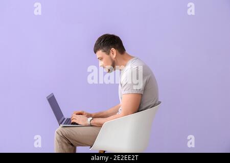 Mann mit schlechter Körperhaltung mit Laptop, während er auf einem Stuhl sitzt Vor farbigem Hintergrund Stockfoto