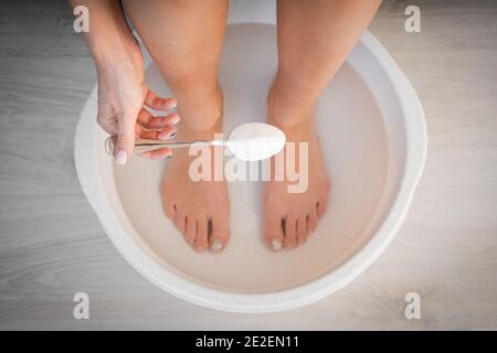 Frau legte Löffel Backpulver in Bad mit heißem Wasser für seine Füße. Hausgemachtes Bad für trockene Füße Haut. Stockfoto
